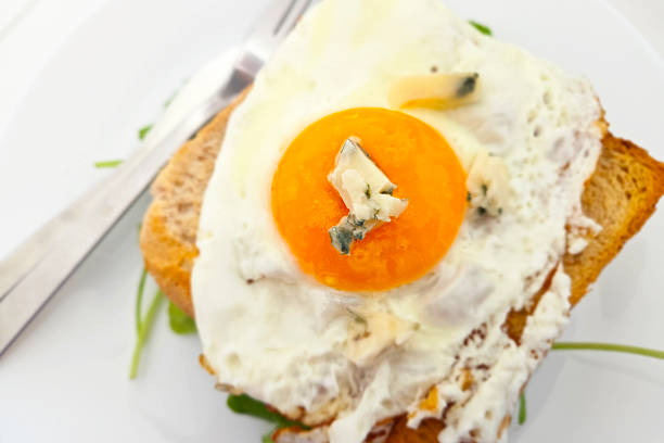 A delicious breakfast scene featuring a perfectly fried egg nestled on toasted bread, topped with rich blue cheese. crisp greens add a touch of freshness and color, ideal for food photography and culinary inspiration.