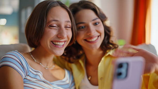 istock Cheerful girlfriends waving smartphone webcam having video call in home closeup. 2252947004