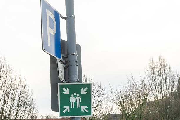 A blue pedestrian zone sign featuring icons of a person walking, a child playing with a ball, a car, and a house. The sign is mounted on a pole in front of a modern residential building, indicating a shared living and walking space in an urban area.