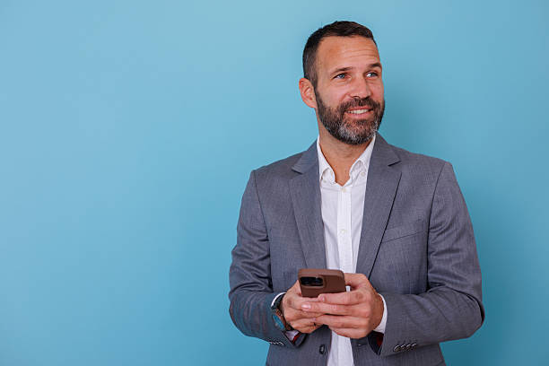 istock Business professional man smiling holding smartphone on blue studio background with copy space 2252955862