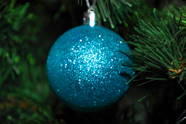 istock ​A glowing blue ball, densely covered with fine glitter, hangs among the thick coniferous branches of a Christmas tree. 2252958960