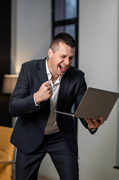 istock Businessman celebrating achievement while standing in office with laptop 2252961729