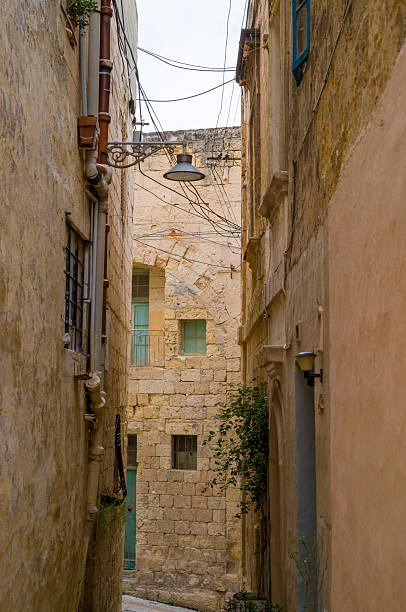 A narrow street in Mdina, Malta, showcases the city's historic architecture. The buildings' aged stone and colorful windows create a unique atmosphere, inviting exploration.