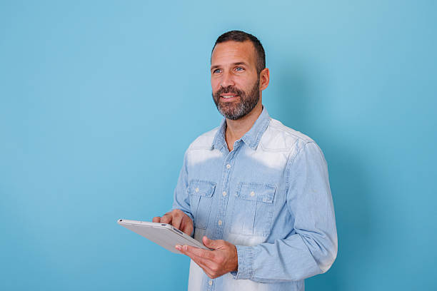 istock Bearded man using digital tablet, smiling and looking away on blue background, thinking about future ideas 2252970938
