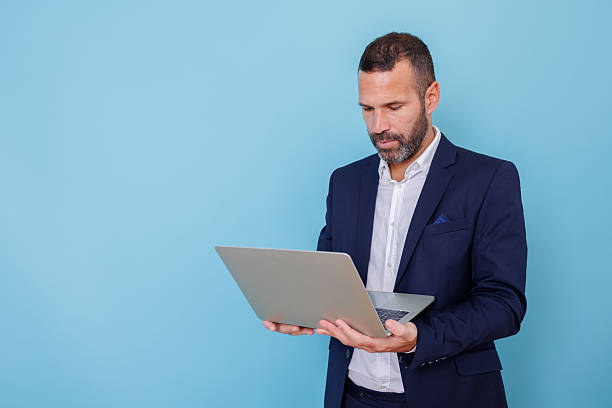 istock Businessman networking on laptop, standing against blue background with copy space, focused on work 2252971510