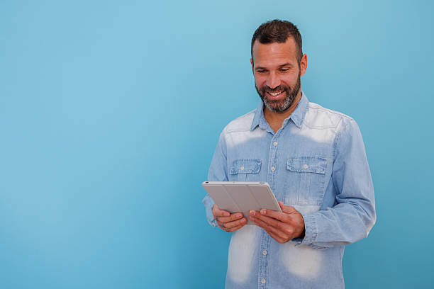 istock Happy man in a denim shirt browsing content on a digital tablet, enjoying connection and modern technology 2252972346