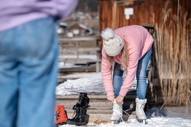 During a winter school holiday trip, a mother and daughter sit on the steps of a lakeside hut on a natural ice rink Weissensee in the Austrian Alps, getting ready to ice skate.