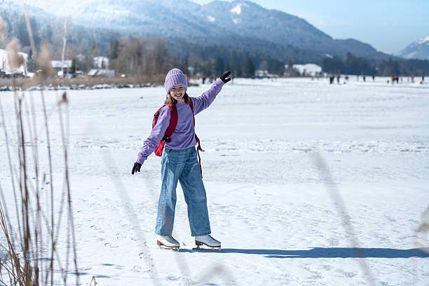 A girl in a purple sweater skates on the natural ice rink Weissensee in the Austrian Alps, warming up around a red backpack.