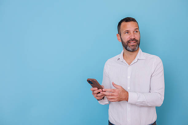 istock Mid adult man holding smartphone looking away thinking, business professional developing new ideas, copy space 2252979505