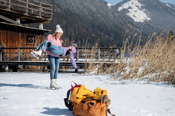Mother and daughter skate on the natural ice rink Weissensee in the Austrian Alps, warming up, making mischief, joking, daughter doing a handstand.