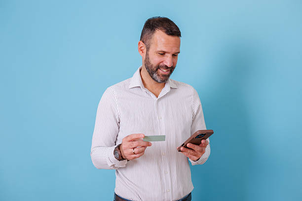 istock Man smiling using mobile phone for online shopping and secure credit card payment on blue background 2252982141