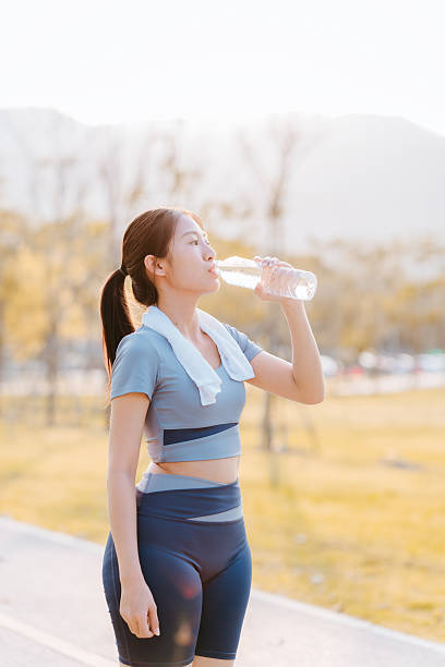 An Asian woman drinks water after exercising in a park.
