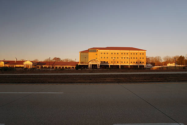 John J. Pershing VA Medical Center is seen from across the roadway in warm late-afternoon light in Poplar Bluff, Missouri. The multi-story main building features a red roof, symmetrical façade, and a central entrance canopy, with flanking wings and surrounding trees anchoring the medical campus in a suburban landscape. The facility serves veterans from Southeast Missouri and neighboring regions, reflecting the role of federal healthcare infrastructure in smaller American cities. Poplar Bluff, Missouri USA November 27, 2025