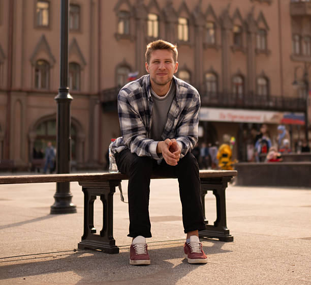 istock A man in a checked shirt sits thoughtfully on a bench near a striking cathedral structure as the sun sets, casting warm light 2252989139