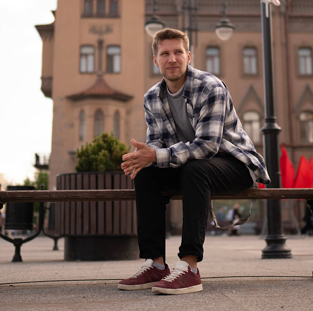 istock A man in a checked shirt sits thoughtfully on a bench near a striking cathedral structure as the sun sets, casting warm light 2252989152