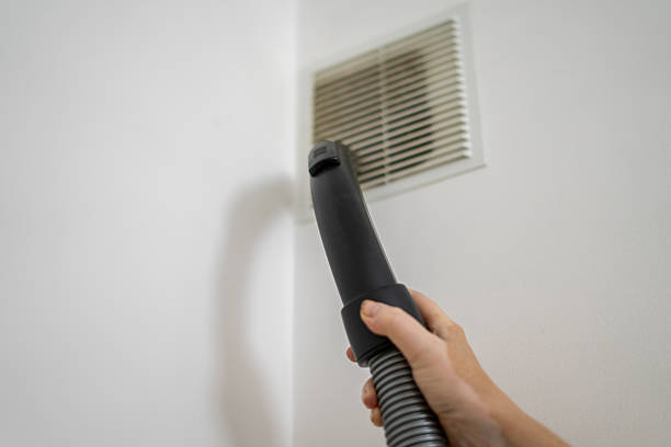 istock A hand holds a vacuum cleaner attachment directed towards a vent cover while performing cleaning tasks to improve indoor air quality in a residential space. 2252992530