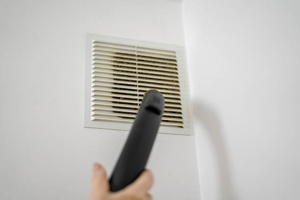 istock A hand holds a vacuum cleaner attachment directed towards a vent cover while performing cleaning tasks to improve indoor air quality in a residential space. 2252992533