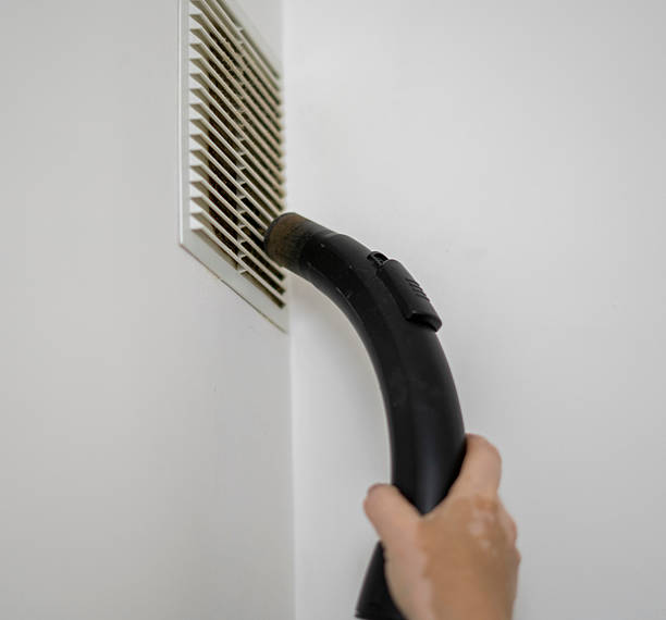 istock A hand holds a vacuum cleaner attachment directed towards a vent cover while performing cleaning tasks to improve indoor air quality in a residential space. 2252992538