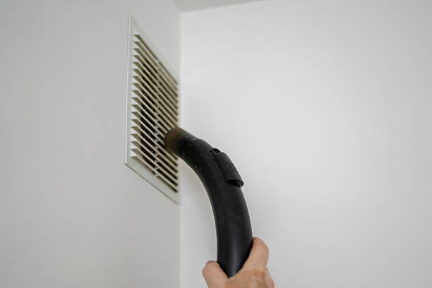 istock A hand holds a vacuum cleaner attachment directed towards a vent cover while performing cleaning tasks to improve indoor air quality in a residential space. 2252992542