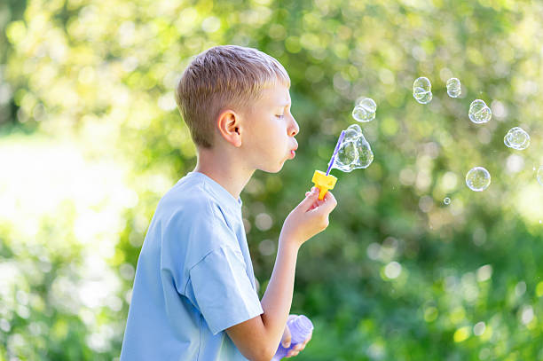 istock Teen boy blowing soap bubbles in summer park 2253000741