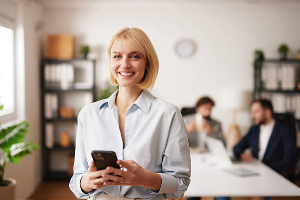 istock Business person smiles while using phone in modern office during work hours with colleagues in background engaged in tasks 2253008124