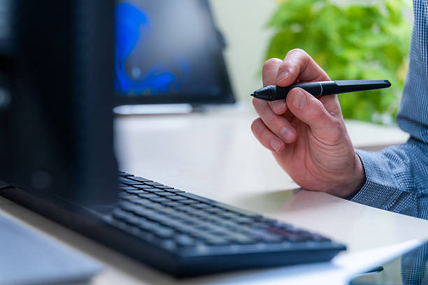 Hand Holds Stylus Near Computer Keyboard In Office Setting, Suggesting Digital Work With Editing, Writing, And Design Tasks Using Modern Technology Tools For Productivity And Workflow.