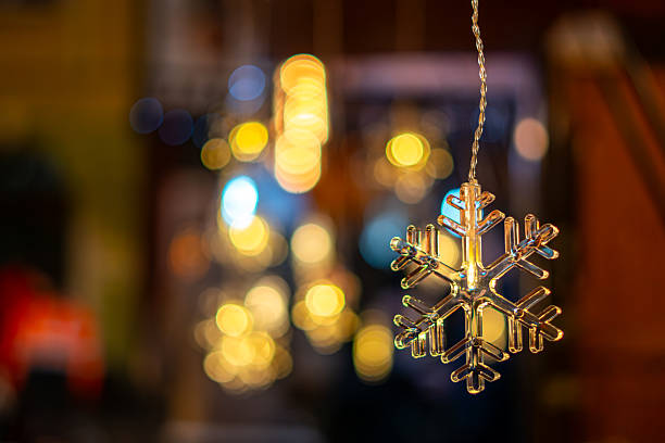 Glass snowflake ornament hanging on string with blurred festive lights background at Christmas market