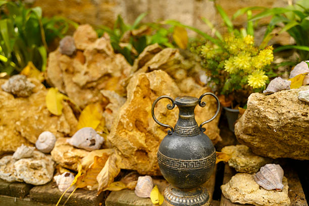 Yellow shell rock stones featuring a vintage copper vase, sea shells, and green plants. Concept of garden decoration, rustic outdoor style, and natural stone textures.