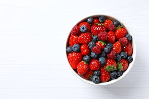 istock Different fresh ripe berries in bowl on white table, top view 2253032127