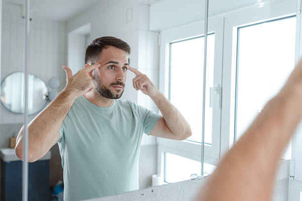 istock Man performs morning self-care routine in the bathroom, looking at his reflection in the mirror 2253034287