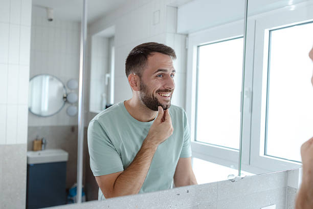 istock Smiling man in a bathroom mirror checking his grooming during a morning routine 2253034331