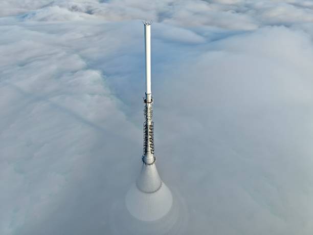 Broadcast Mast Emerging Through Low Fog With Antenna Arrays And Sunlight Glinting, Mountain Ridge Hinted