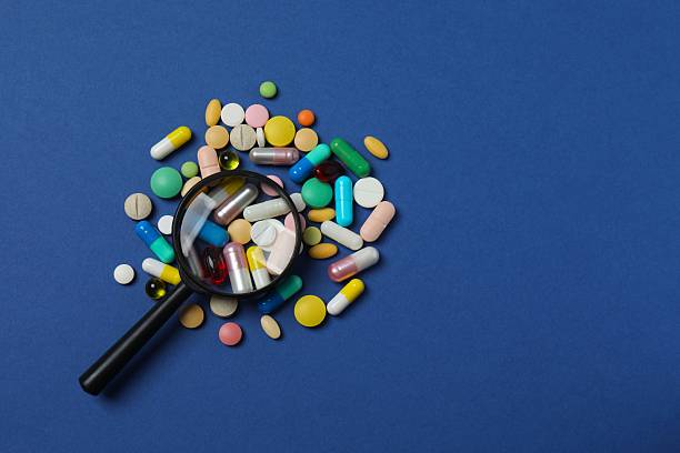 istock Various pills with magnifying glass on blue background 2253038090