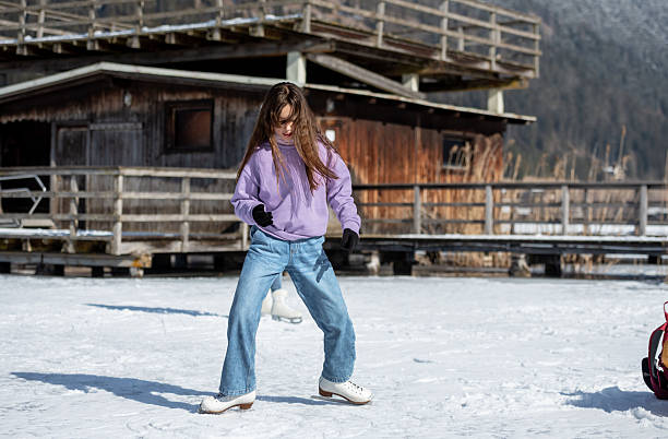 A girl in a purple sweater skates on the natural ice rink Weissensee in the Austrian Alps, warming up around a yellow backpack.