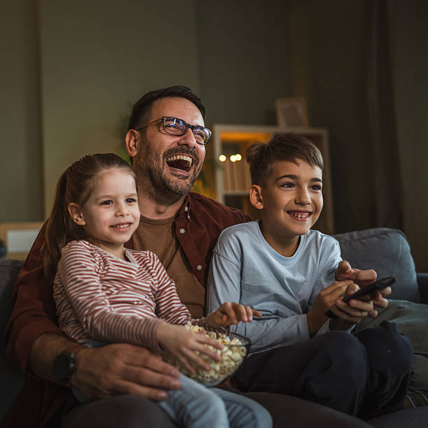 istock Father with children watching tv on sofa eating popcorn 2253047215