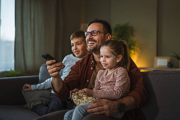 istock Father with children watching tv on sofa eating popcorn 2253047295