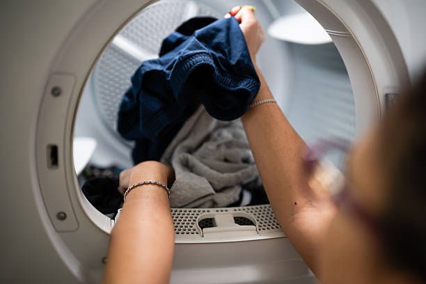 istock Woman loading clothes into a laundry dryer 2253048571