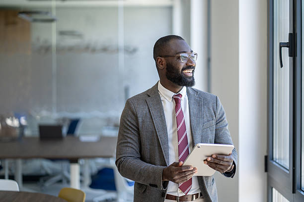 istock Smiling businessman holding digital tablet looking out office window 2253051038