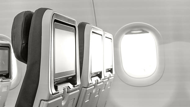Airplane interior featuring empty passenger seats with personal screens and a bright window, creating a serene travel atmosphere with copy space, toned with Colour of the year Cloud Dancer.