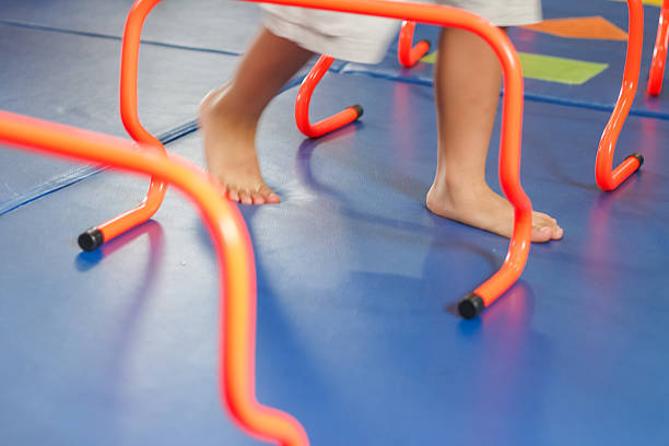 A child performing a physical exercise involving stepping over small orange agility hurdles