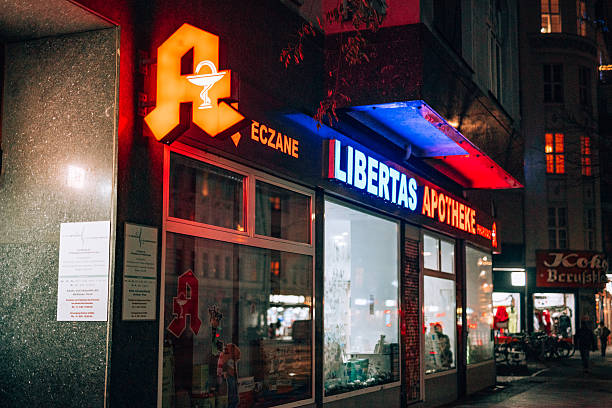 Berlin, Germany – December 21, 2025: Exterior view of Libertas Apotheke pharmacy with illuminated signage and storefront windows on a city street at night.