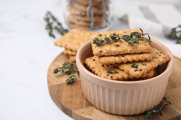 istock Cereal crackers with flax, sesame seeds and thyme in bowl on light table, closeup. Space for text 2253061064