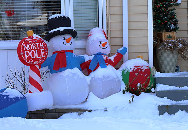 Two snowmen standing shoulder to shoulder, leaning against a house wall, smiling as if greeting. Festive winter decoration scene.