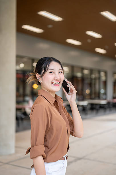 istock Asian woman student talking on phone call looking ahead while standing sideway in open air building. 2253063076