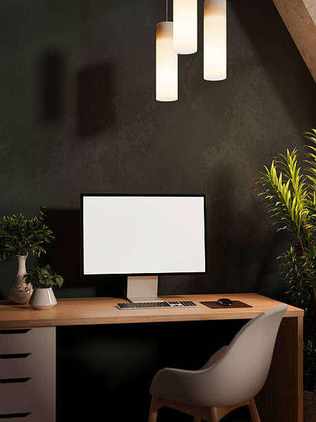 istock White screen computer on wooden drawer table and chair under hanging lamp aside wall in dim lit room 2253065007