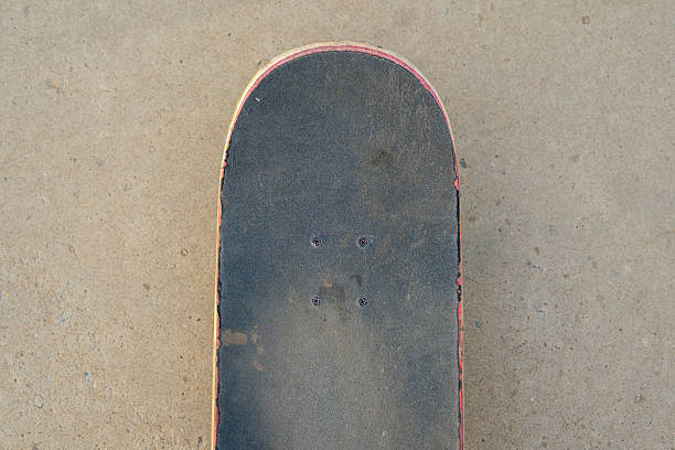 istock A skateboard lays on a smooth concrete surface, surrounded by skateboarders enjoying their evening at a vibrant skatepark as the sun sets behind them. 2253065954