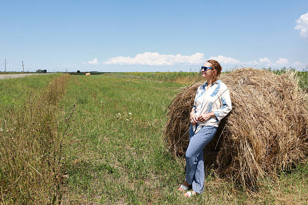 Woman relaxing in a rural landscape, leaning against a haystack. Idyllic scene for country living, summer travel, and agricultural concepts.