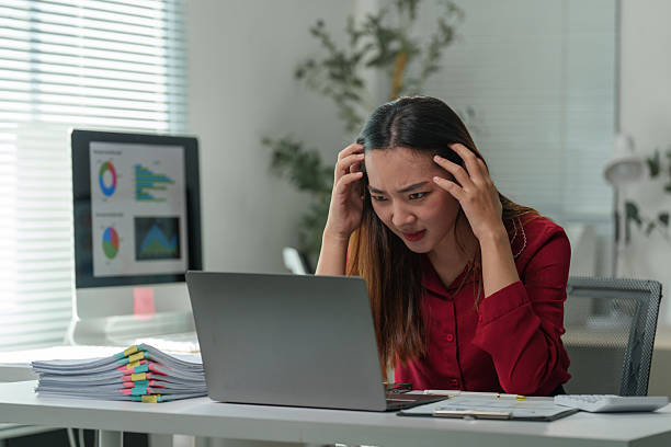 istock Young asian businesswoman is having a headache and feeling stressed while working on a laptop at her desk in the office, looking at the screen with a worried expression 2253072517