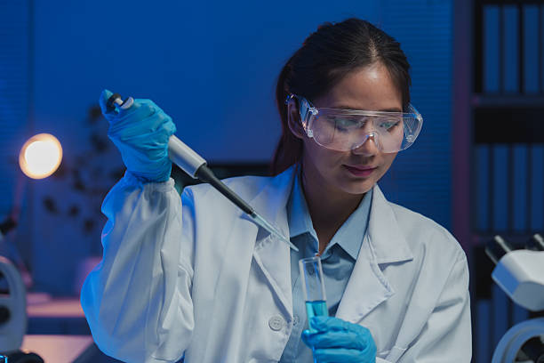 istock Young female scientist wearing lab coat and protective glasses, carefully using a pipette to transfer blue liquid into a test tube in a modern, illuminated laboratory 2253073106
