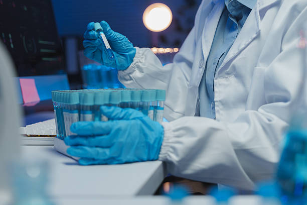 istock Scientist wearing a lab coat and gloves carefully analyzes a test tube containing a blue liquid, working diligently in a modern laboratory setting filled with advanced equipment 2253073149